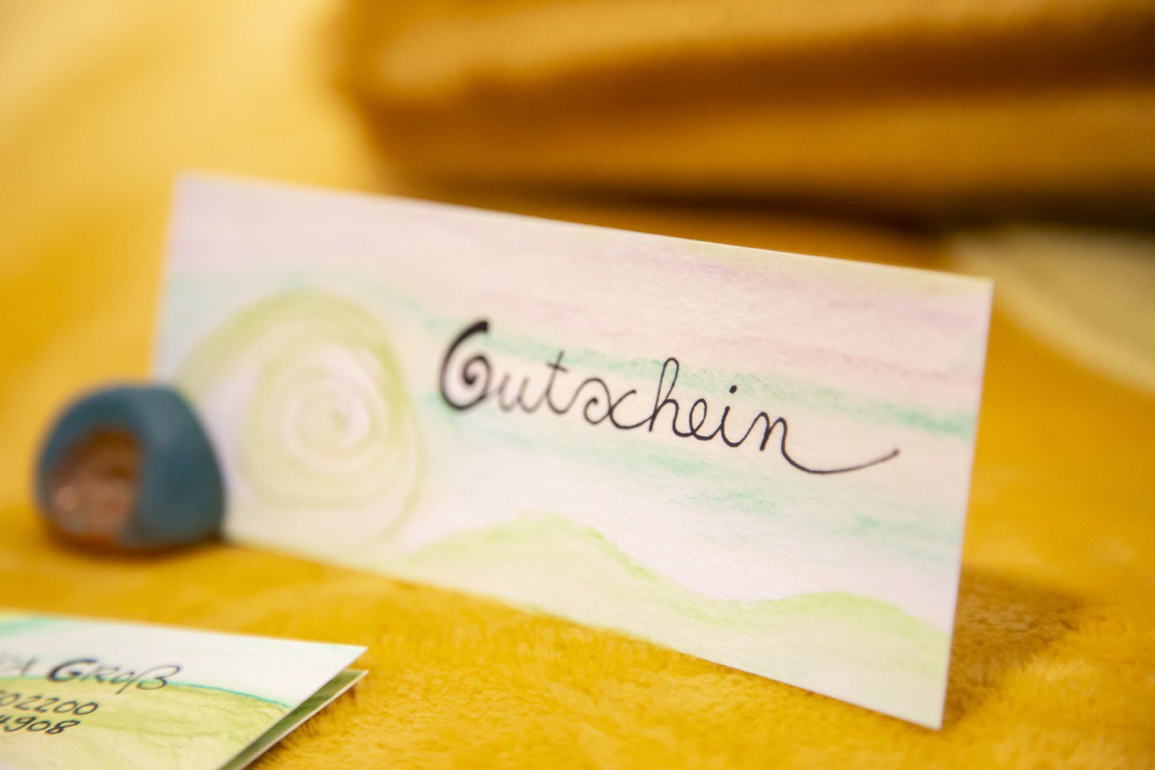 Ein kleines handbemaltes Schild auf dem steht "Gutschein" steht auf einer gelben Decke